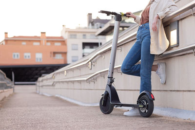 Cropped view of unrecognizable young woman leaning on the railing holding a electric scooter 