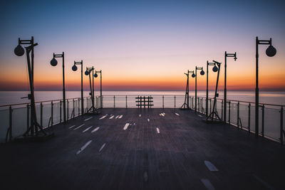 Street lights on pier by sea against sky during sunset