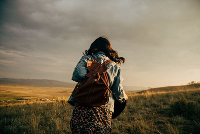 Rear view of woman with backpack walking on grass against sky