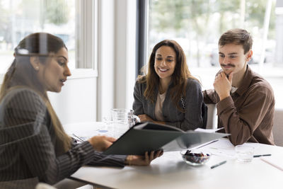 Female real estate agent showing floor plan to smiling customers in office