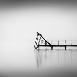 Silhouette bridge over sea against clear sky