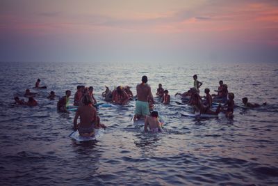 People enjoying in sea against sky during sunset