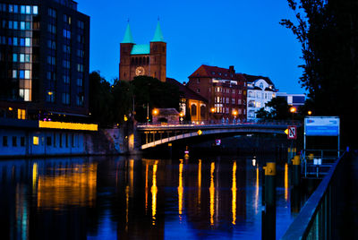 Illuminated bridge over river by buildings against sky at night