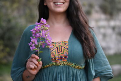 Midsection of smiling young woman holding purple flowers while standing outdoors