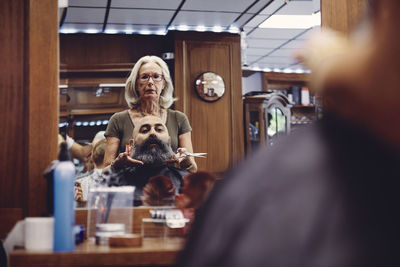 Woman cutting bald man beard in hair salon