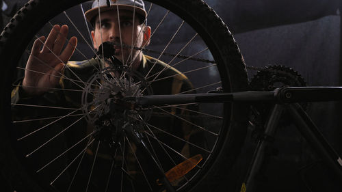 A bike mechanic wearing a baseball cap and shirt repairs a bicycle in a workshop a man spins a wheel