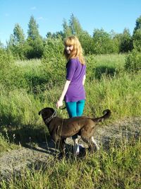 Full length rear view of woman with dog standing on field