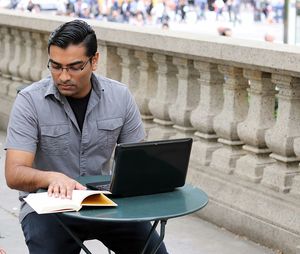 Young man with laptop looking towards diary at sidewalk cafe