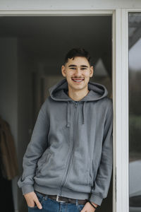 Portrait of smiling teenage boy with hand in pocket standing at doorway