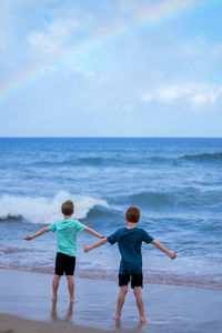 Young boys playing in the waves with a rainbow over the ocean on ka'anapali beach in hawaii. 