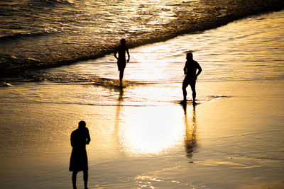 Silhouette friends walking on beach during sunset