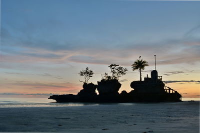 Silhouette rocks on beach against sky during sunset