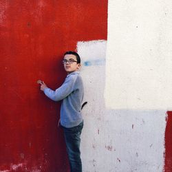 Side view of young man standing against red wall