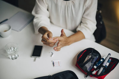 Midsection of businesswoman doing blood sugar test at table in office