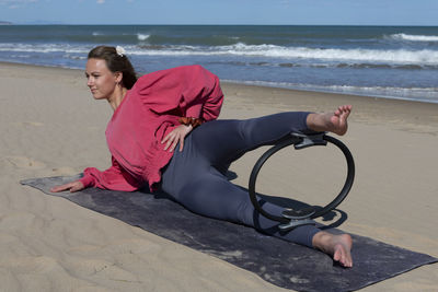 Beautiful woman exercising on the beach with pilates ring
