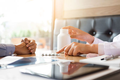 Cropped hands of doctor prescribing medicine to patient on desk