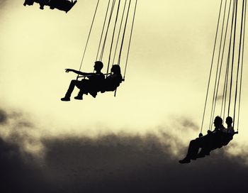 Low angle view of silhouette men sitting against sky