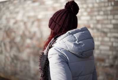 Close-up of woman wearing warm clothing while standing against brick wall