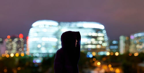 Woman looking at illuminated city against sky at night