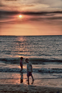 Full length of men on beach against sky during sunset