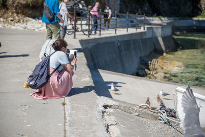 Rear view of woman photographing ducks on footpath