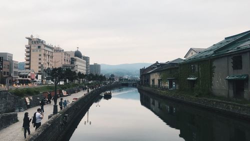 People walking by canal in city against sky