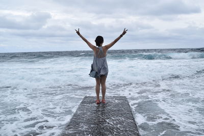 Rear view of woman gesturing peace sign on pier against cloudy sky