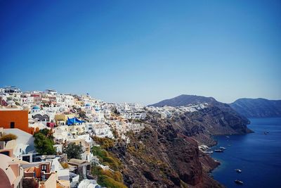 Cityscape by sea against clear blue sky