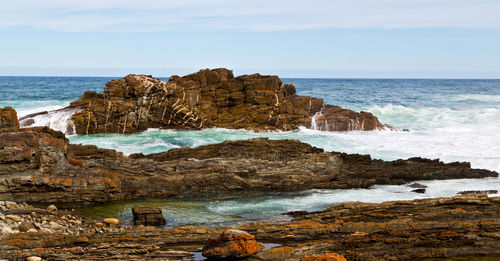 Rocks on shore by sea against sky