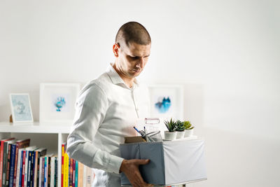 Young man looking away while standing against white wall