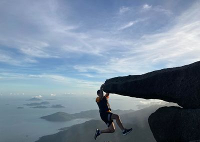 Rear view of man hanging on mountain cliff against sky