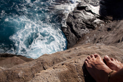 Low section of man standing by sea on rock during sunny day