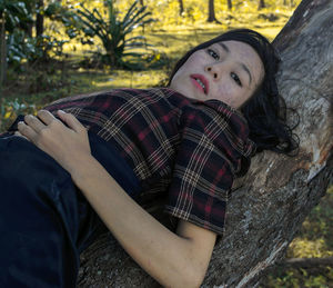 Portrait of young woman lying down on tree trunk