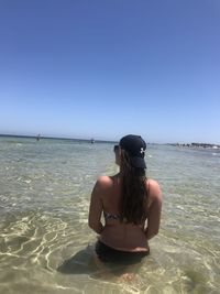 Rear view of woman sitting in sea against clear sky