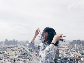 Rear view of woman standing by cityscape against sky