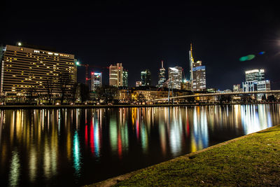 Illuminated buildings by river against sky at night