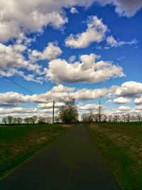 Road passing through field against cloudy sky