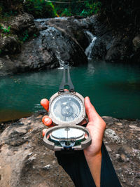 Cropped hand holding navigational compass against waterfall in forest