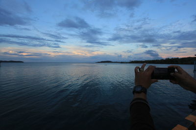 Man photographing sea against sky during sunset