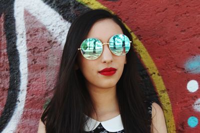 Portrait of young woman wearing sunglasses against wall