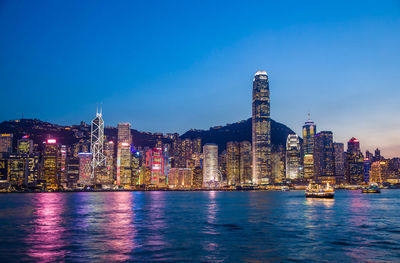 Illuminated buildings by river against sky at night