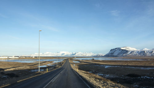 Road leading towards snowcapped mountains against sky