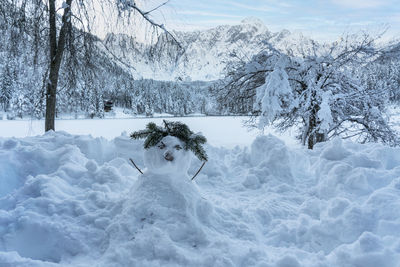 A snowman on the shore of lake fusine, tarvisio, frozen in winter