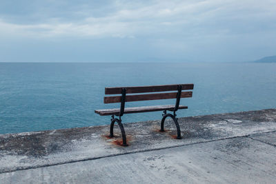 Empty bench on shore by sea against sky