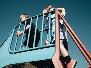 Low angle view of kids on slide against clear blue sky