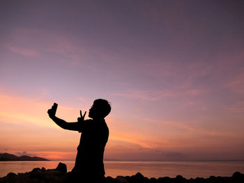 Silhouette woman standing at beach during sunset