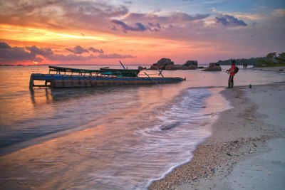 Man fishing at beach during sunset