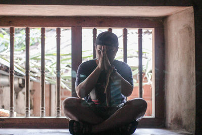 Man with hands clasped sitting on window sill