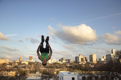 Full length of man jumping upside down against sky in city