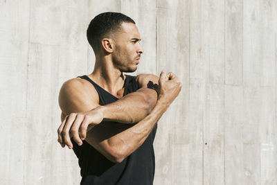 Side view of man with arms raised standing against wall